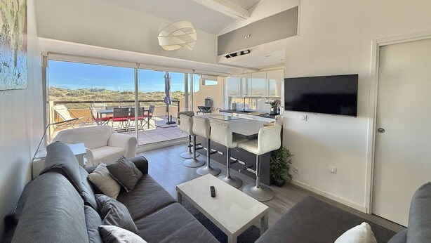 Una sala de estar moderna con sofá, mesa de centro, televisor y balcón con mobiliario exterior.