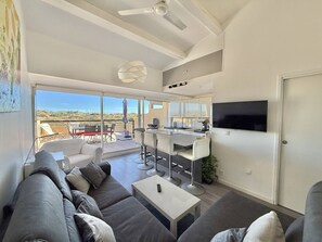 Ein modernes Wohnzimmer mit einer Couch, einem Couchtisch, einem Fernseher und einem Balkon mit Gartenmöbeln.