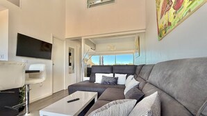 Una sala moderna con un sofá gris, una mesa de centro blanca y un televisor montado.