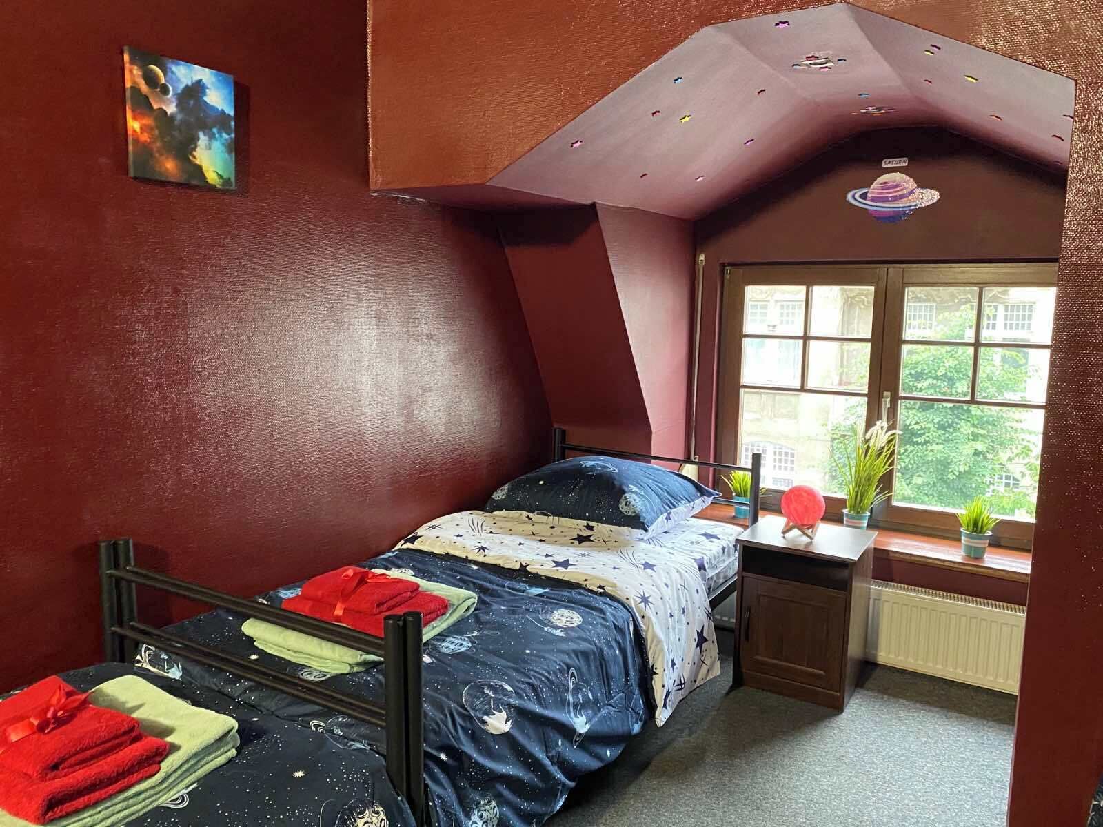 A bedroom with a bed, a window, a desk, and a small plant.