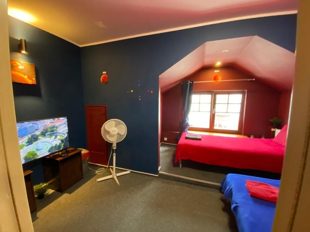 A room with a TV, a fan, a bed, and a window.