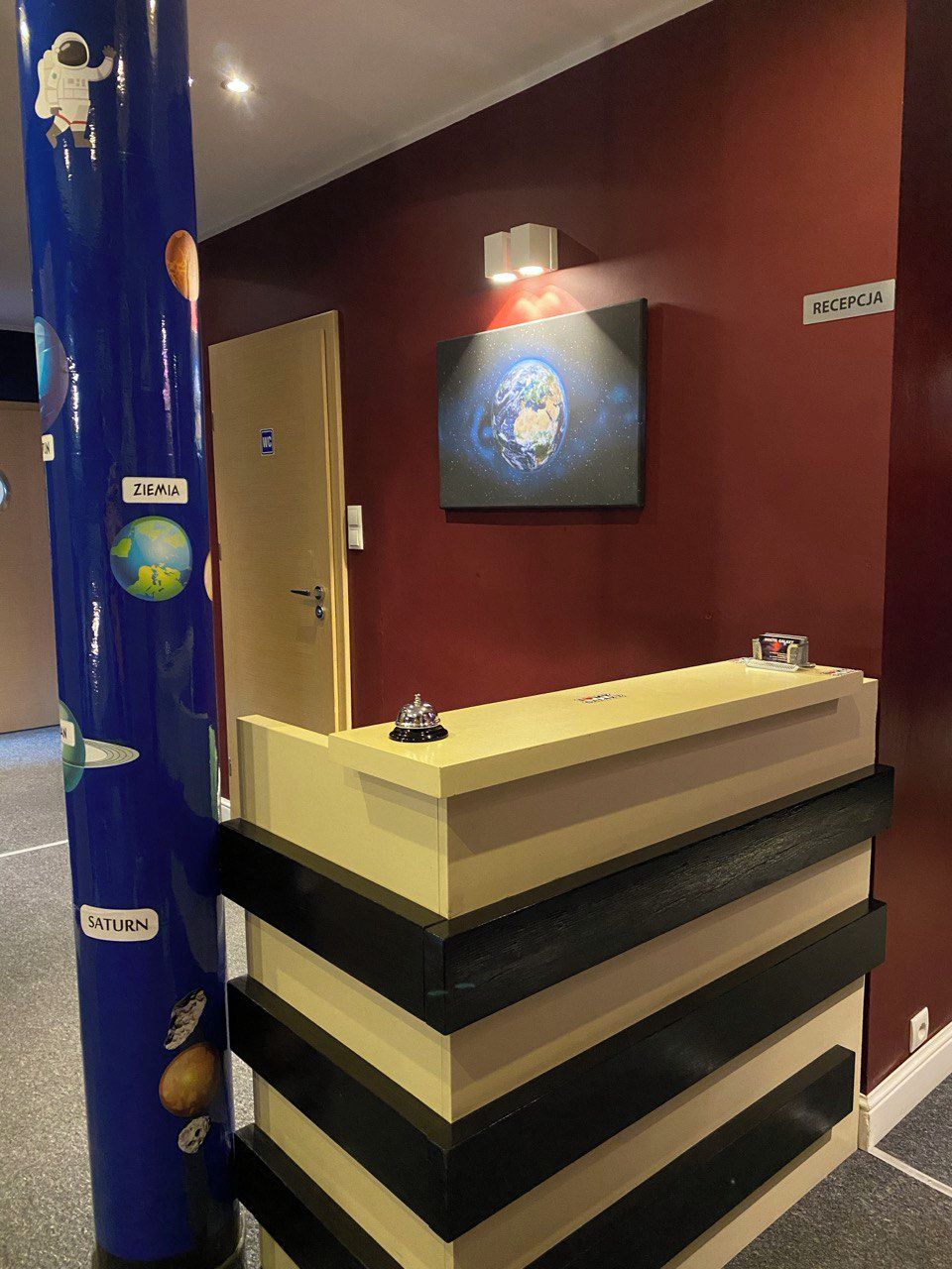 A reception desk with a 'RECEPTION' sign, a wall-mounted globe, and a blue pillar with space-themed decorations.