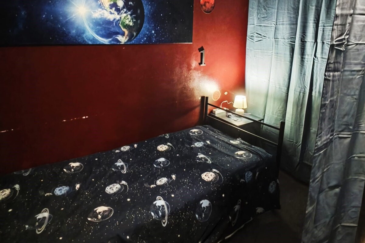 A room with a bed, a wall-mounted TV, a lamp, and a curtain.