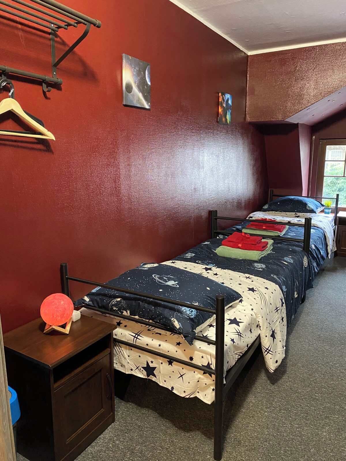 A bedroom with two beds, a wooden nightstand, a hanging rack, and a small window.