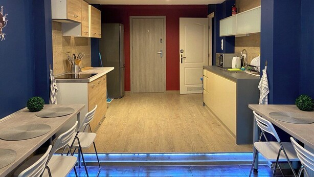 Een compacte keuken met een centraal eiland, een eethoek met stoelen, en een deur naar een andere kamer.