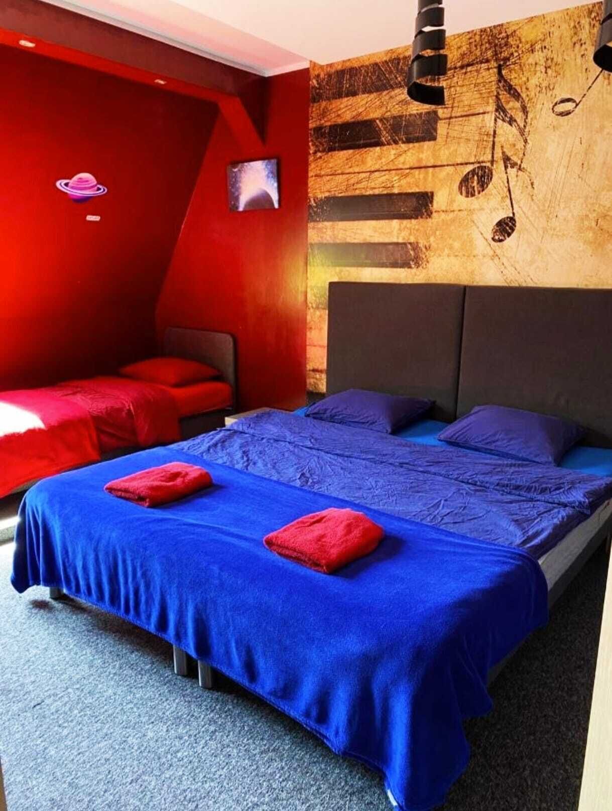 A room with a bed, a red wall, a television, and a wall with musical notes.