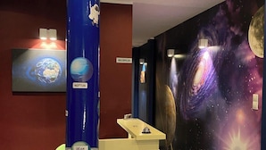 Een receptiebalie met een muurschildering met een kosmisch thema, een blauwe kolom met planeetillustraties en een trap naar een hoger niveau.
