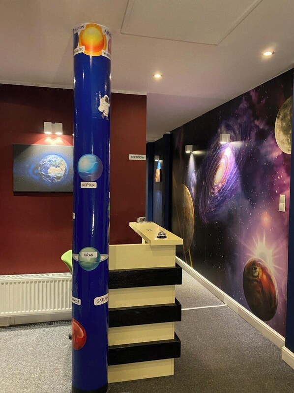 A reception desk with a cosmic-themed mural, a blue column with planetary illustrations, and a staircase leading to an upper level. - Hostel Galaxy (Gdańsk)