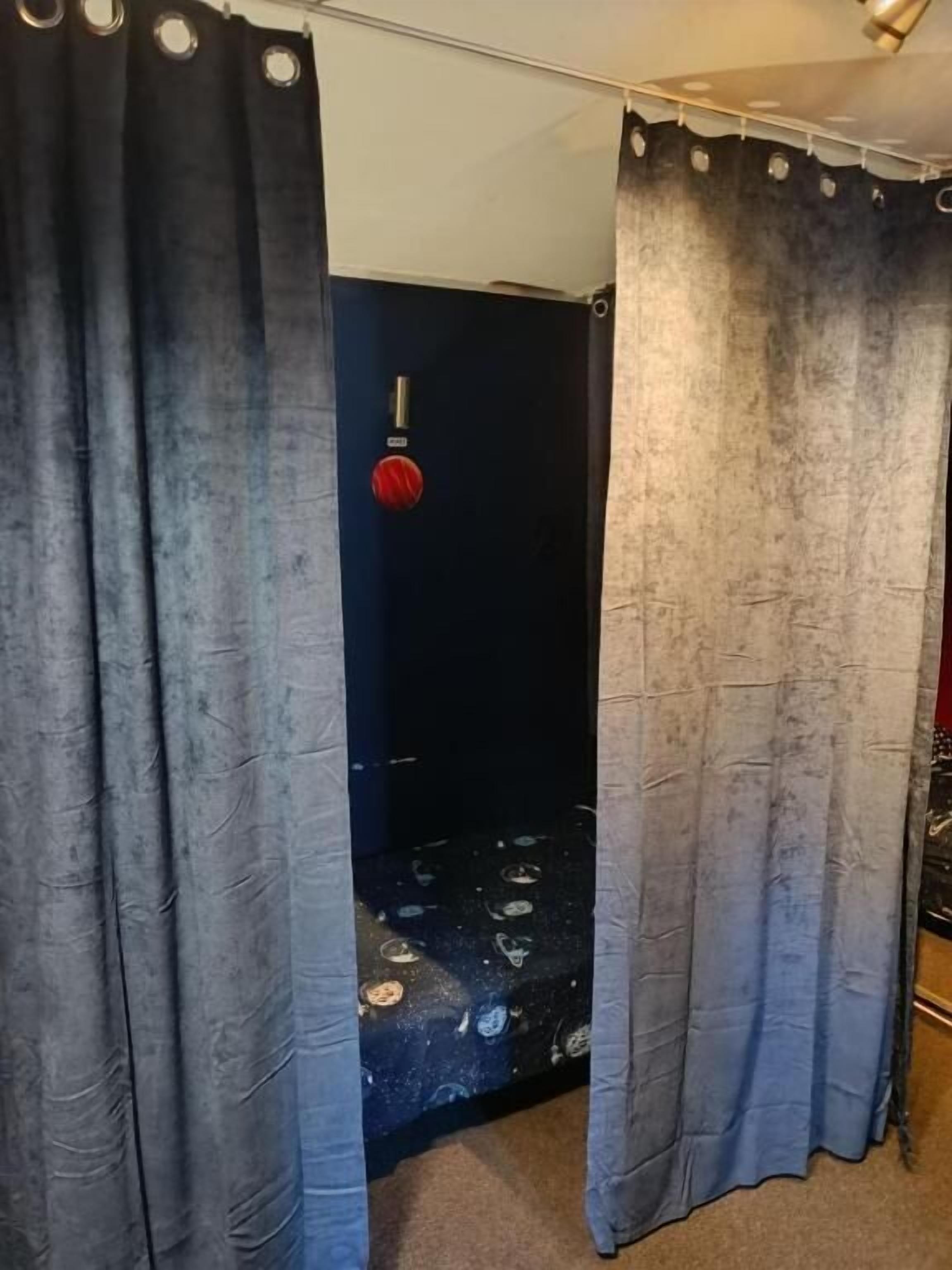 A room with a shower area, a door with a red handle, and a curtain partially drawn.