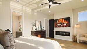 A bedroom with a large bed, a ceiling fan, a fireplace, and a TV mounted on the wall. - Lake on Winnetka Dream Home - Trinity Grove & Downtown Dallas (Dallas)