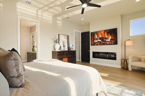 A bedroom with a large bed, a ceiling fan, a fireplace, and a TV mounted on the wall. - Lake on Winnetka Dream Home - Trinity Grove & Downtown Dallas (Dallas)