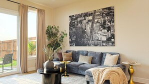 A living room with a sofa, a coffee table, a side table, a large cityscape artwork, a potted plant, and a sliding glass door. - Lake on Winnetka Dream Home - Trinity Grove & Downtown Dallas (Dallas)