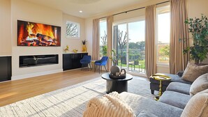 A living room with a fireplace, a large TV, a sofa, and a dining area with chairs. - Lake on Winnetka Dream Home - Trinity Grove & Downtown Dallas (Dallas)