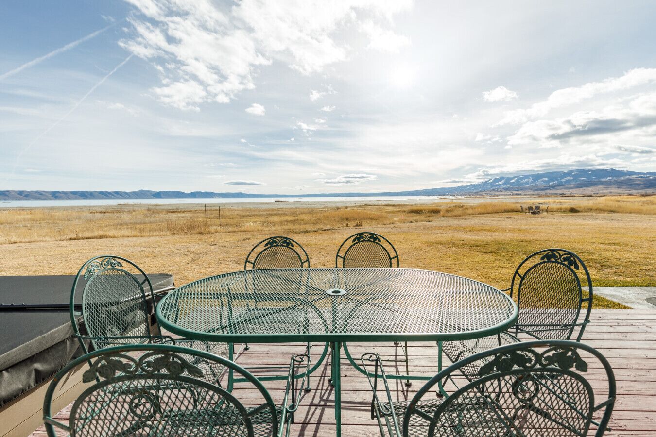 A metal table and chairs on a deck with a view of a flat landscape and mountains in the distance.