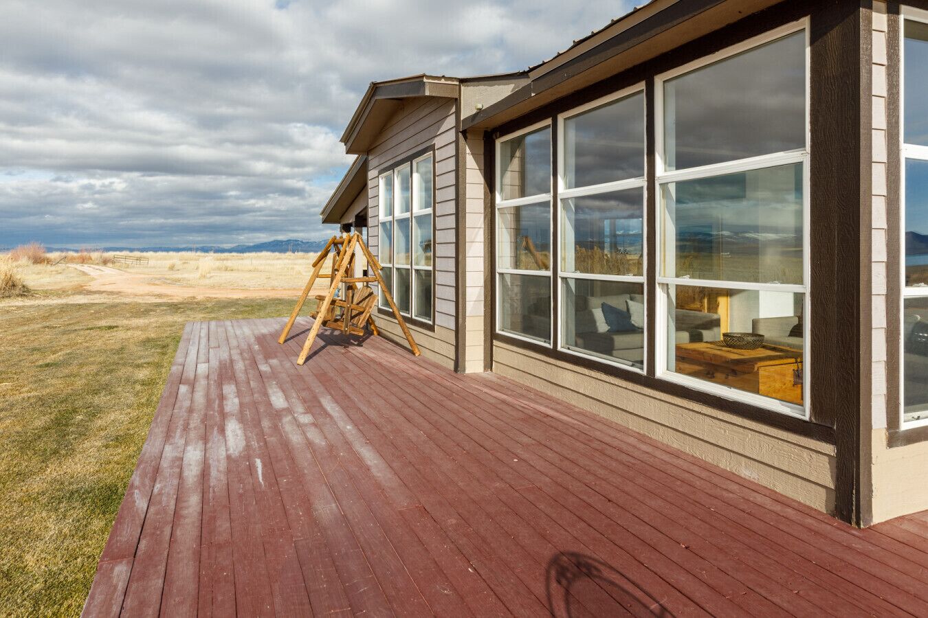Una terraza de madera con un columpio, ventanas amplias y vistas del paisaje.