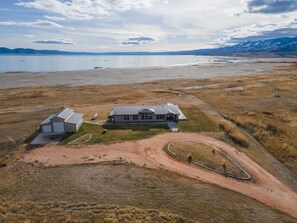 An aerial view of a property with a large house, a barn, and a dirt road leading to a body of water.