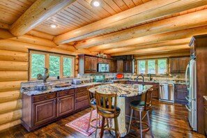 Eine Kücheneinrichtung im Chalet-Stil mit Holdekor, einer Granitarbeitsplatte und einer großen Kochinsel mit Barhocker.