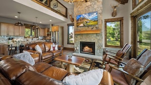 Amplia sala de estar con mobiliario de cuero, chimenea y un ventanal con vistas a un paisaje pintoresco.