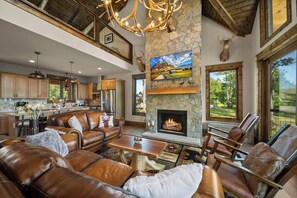 A spacious living room with leather furniture, a fireplace, and a large window overlooking a scenic landscape. - Safe Haven at Eagles Nest - views, hot tub, firepit, fireplace, game table (Banner Elk)
