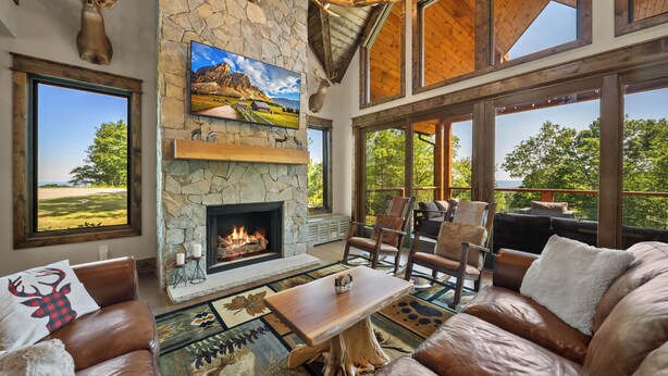 Una sala de estar acogedora con chimenea de piedra, muebles de cuero y amplias ventanas con vistas al exterior.