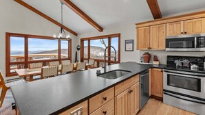 A kitchen with wooden cabinets, a large island with a sink, a microwave, and an oven. There are large windows offering a view of the outdoors. - Daisy Ridge - Expansive Mountain View, Pets OK, Beech Mtn Club option, foosball, arcade (Beech Mountain)