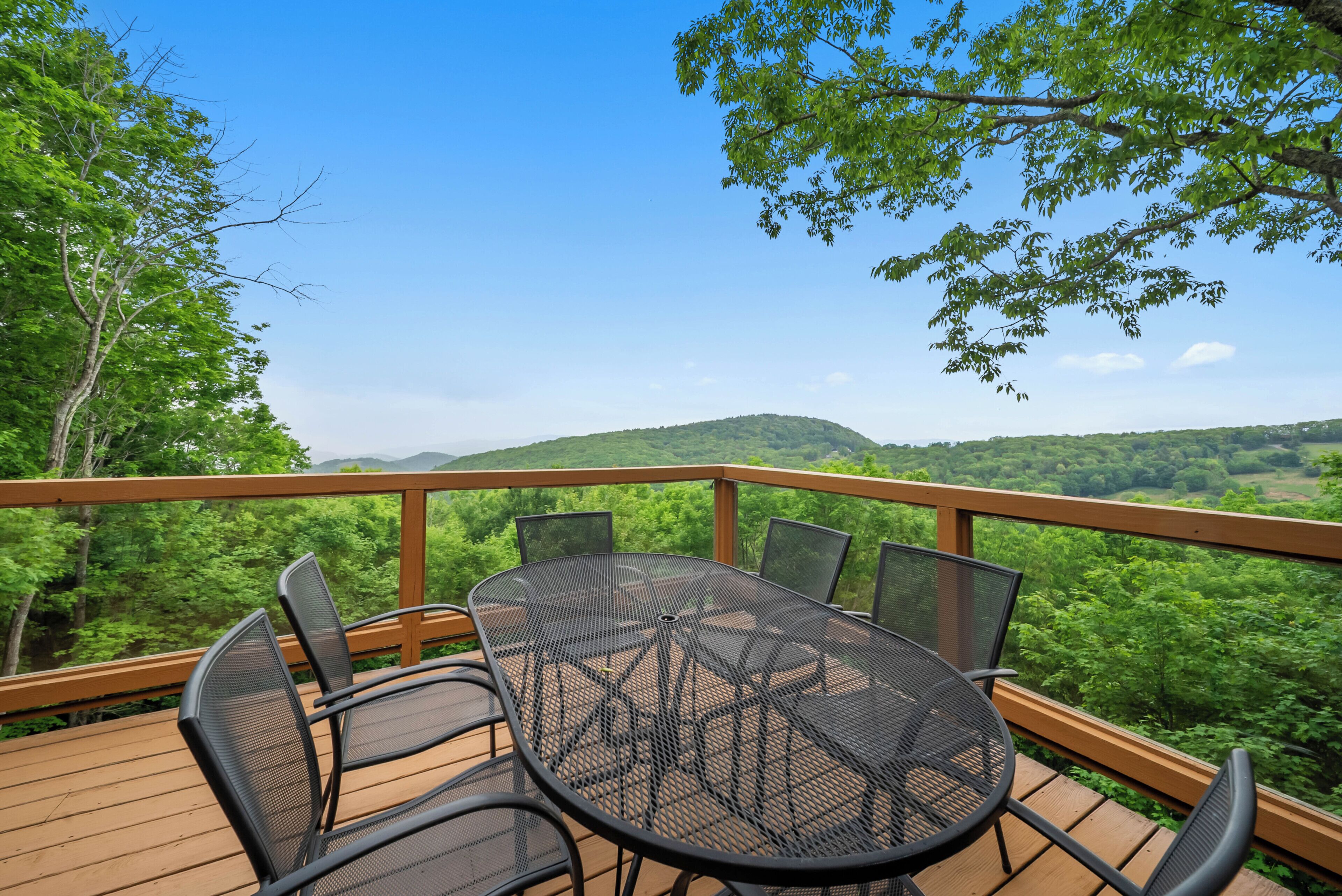 A deck with a table and chairs, overlooking a forested landscape.