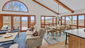 A spacious living area with a large window, a dining table, and a sofa. - Daisy Ridge - Expansive Mountain View, Pets OK, Beech Mtn Club option, foosball, arcade (Beech Mountain)