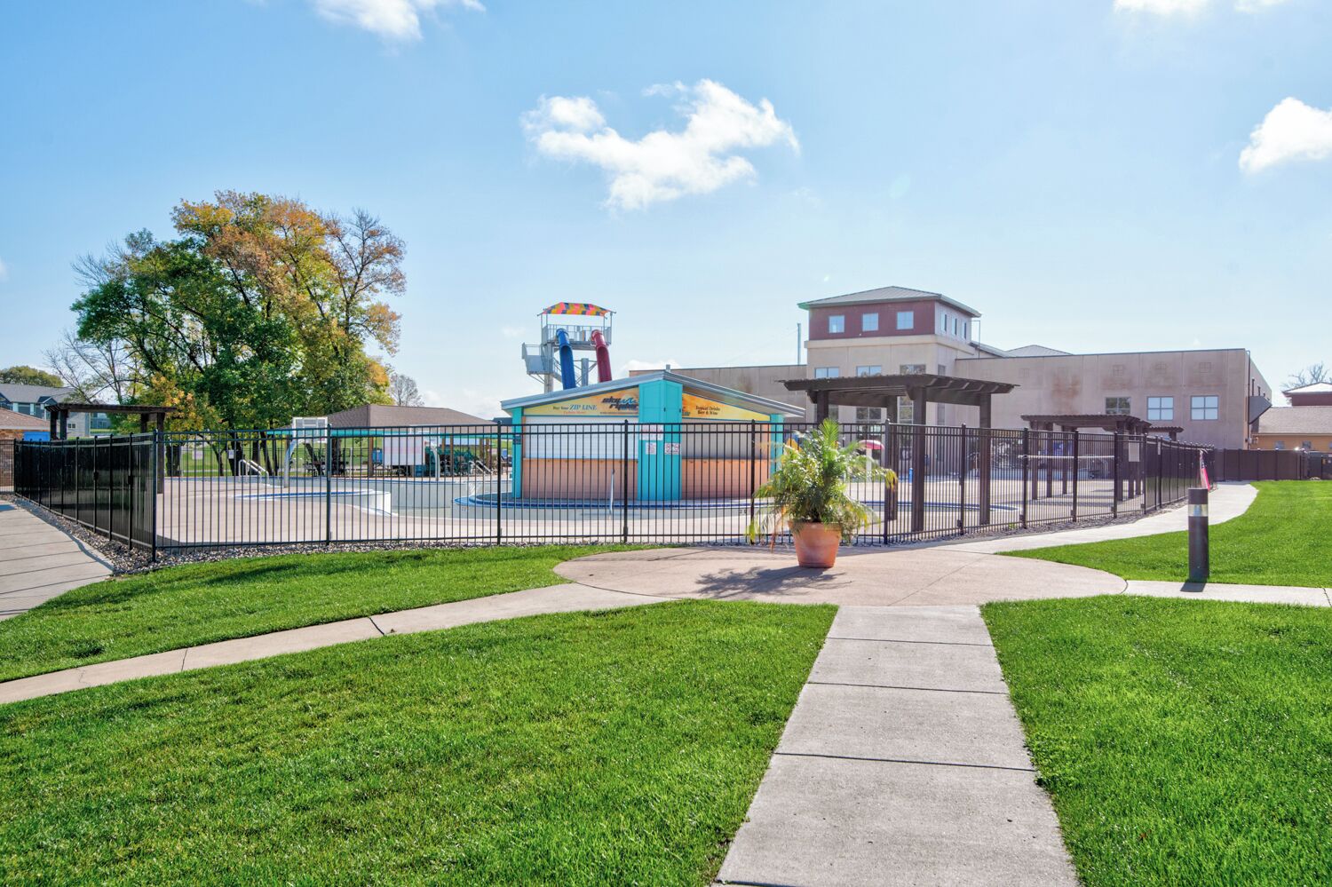 Ein eingezäunter Außenbereich mit Spielplatz, ein Gebäude mit flachem Dach und einem klaren Himmel.