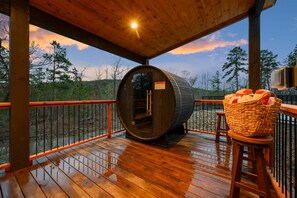 Eine Holterrasse mit Sauna, einem Korbwägelchen und Blick auf Bäume.