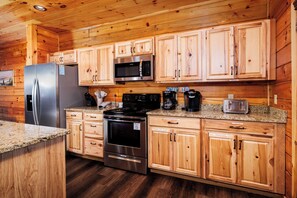 A kitchen with wooden cabinets, stainless steel appliances, granite countertops, and a coffee station. - Fiddler's Friend - Hot Tub Soaks, Theater Movie Nights & Game Room Competitions (Pigeon Forge)
