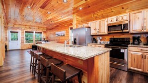 Ein Holzblockhaus-Innenraum mit einer Küche, die sich durch Granit-Arbeitsplatten, Edelstahlgeräte und Holzschränke auszeichnet.
