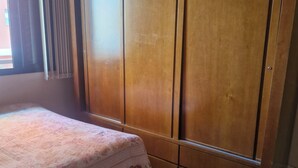 Quarto com cama, guarda-roupa de madeira e janela com cortinas.