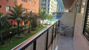 Uma varanda com vista para um edifício, uma piscina e palmeiras.