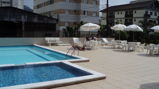 Piscina com deck revestido, cadeiras de lounge brancas e guarda-sóis.