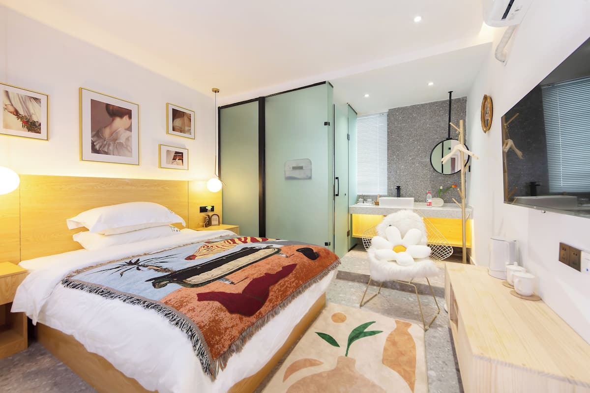 Una habitación de hotel moderna con cama, mesita de noche, televisor de pared y baño visible a través de una puerta abierta.