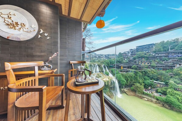A balcony with wooden furniture, a decorative plate, and a view of a traditional village with a river. - 12C Waterfall Stay Furong Main Falls (Xiangxi)