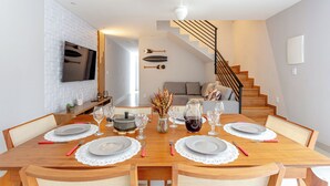 A dining area with a wooden table set for four, a vase with dried flowers, and a staircase leading to another level.