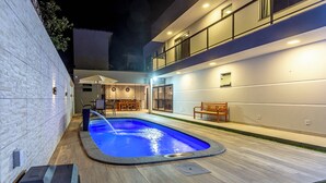 A modern outdoor pool area with a stone wall, wooden deck, and a two-story building with balconies.