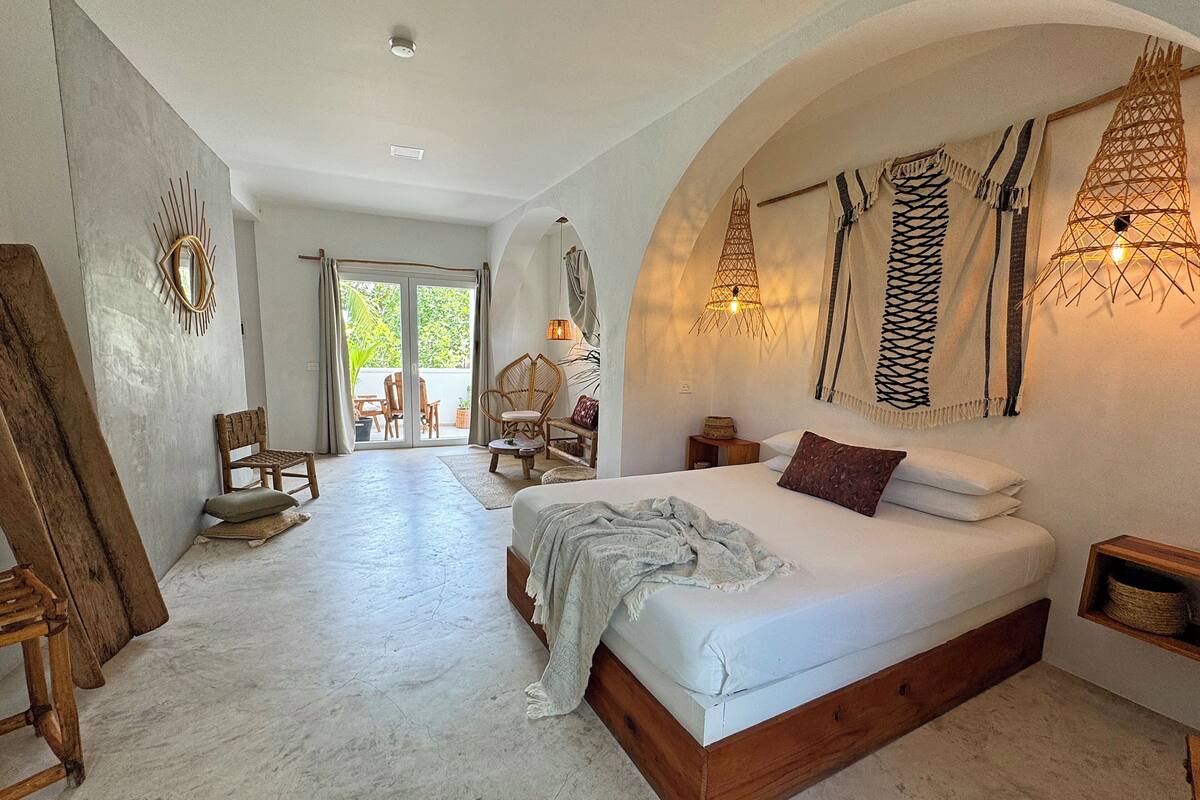 Une chambre avec un grand lit, une chaise en bois, une petite table et une vue sur un espace extérieur aménagé avec des chaises et une table.