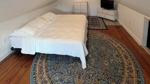 A bedroom with a bed, a TV, a dresser, and a patterned rug.