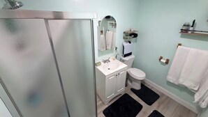 A bathroom with a shower, toilet, sink, and two black rugs on the floor.