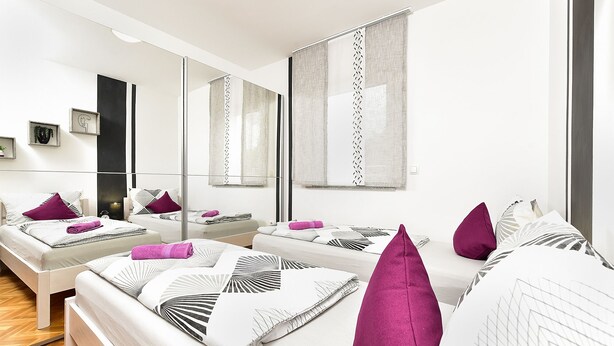Une chambre d’hôtel moderne avec un grand lit, un lit plus petit et un canapé. On y trouve plusieurs oreillers et un miroir.