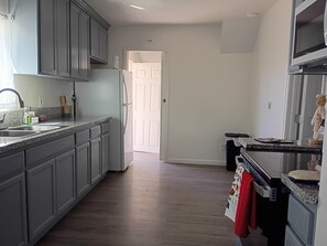 A kitchen with grey cabinets, a stainless steel refrigerator, a microwave, and a sink. - 3-bedroom house in peaceful Fresno with cool AC breeze (Fresno)