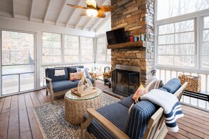 A cozy room with a stone fireplace, a television mounted on the wall, and a large window offering a view of the outdoors. - Family Luxury Lake Michigan Cottage w/ Hot Tub (West Olive)