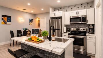 A modern kitchen with white cabinets, stainless steel appliances, a marble island, and a welcome sign.