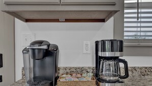 A kitchen with a Keurig coffee maker, a glass coffee pot, and a basket of coffee pods.