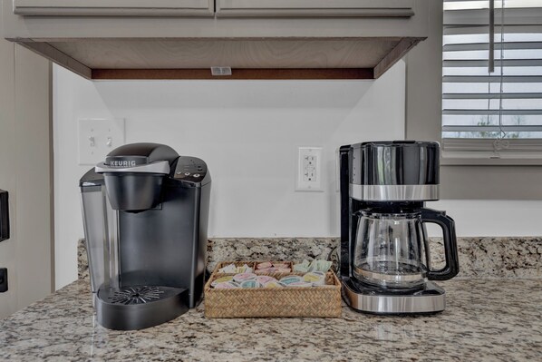 Una cocina con una cafetera Keurig, una jarra de vidrio y un cesto de cápsulas de café.