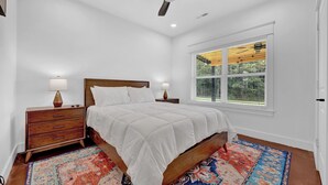 A bedroom with a bed, nightstands, a ceiling fan, a window with blinds, and a patterned rug.