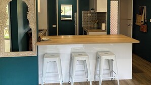 A modern kitchen with a wooden island, white bar stools, and a decorative mirror. - OP 63 - Rest & Recharge at Your Beachside Escape (Coffs Harbour)