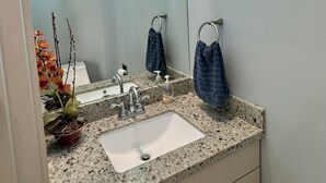 Een badkamer met een granieten aanrecht, een wit wastafel, een spiegel en een raam met een blauw patroon.
